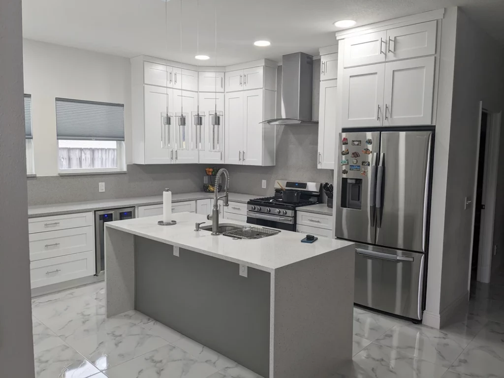 a grey and white themed elegant looking kitchen, a kitchen island waterfall edge design countertop, silver appliances, ice white shaker cabinet door installed