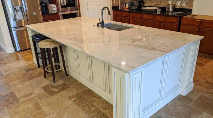 a kitchen island with a marble quartz countertop and signature pearl cabinet door style, and two bar chairs