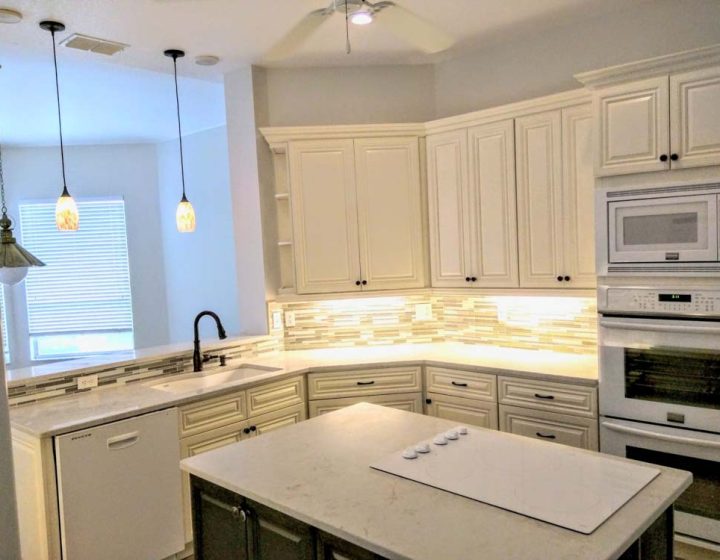 a fully remodeled modern white kitchen that has an island with induction cooktop, white appliances, wood strip backsplash pattern, and K-white cabinet door design