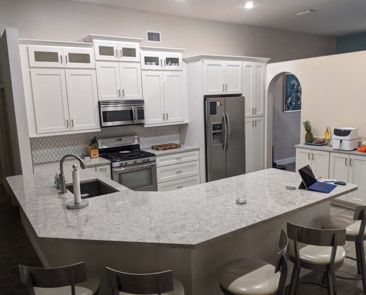 custom ice white shaker kitchen cabinets, silver appliances, granite countertop, and five island chairs